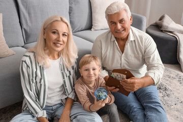 Wall Mural - Little boy with piggy bank and his grandparents at home