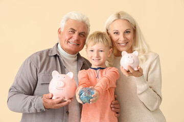 Wall Mural - Little boy with his grandparents and piggy banks on beige background