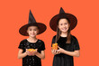 © Pixel-Shot - Cute little girls dressed for Halloween as witches with tasty candies on orange background