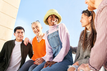 Wall Mural - Multiracial group of diverse guys sitting outdoors having fun. Young multi-ethnic friends enjoying together happy. Smiling people community of colleague students. Modern lifestyle of multicultural.