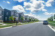 © kosoff - Quiet street in a residential area in the suburbs. Rows of houses along the sidewalk with a green lawn.