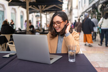 Enthusiastic happy carefree female student prepare freelance project working laptop sitting outdoor cafe laughing joyfully wear glasses enjoy glass water