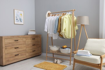 Wall Mural - Wardrobe organization. Rack with different stylish clothes, chest of drawers, armchair and lamp near grey wall indoors