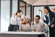 © makibestphoto - Four Asian business people in office look happy and excited. They raise their fists and smile. sit and stand by table with laptops and coffee. They celebrate together. discuss opinions, presentation