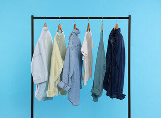 Wall Mural - Rack with stylish clothes on wooden hangers against light blue background