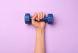© New Africa - Woman holding blue dumbbell on violet background, top view