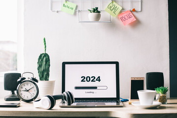 Office desk with 2024 loading bar on laptop screen for happy new year concept