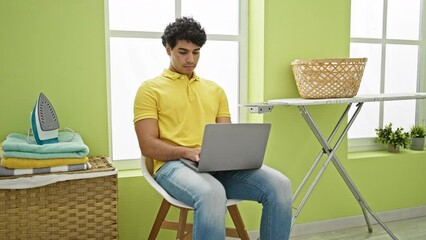 Sticker - Young latin man using laptop waiting for washing machine at laundry room