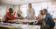 © Gorodenkoff - Adult Education Center: Adult Students Learning in Classroom, Working as Two Teams on a Verbal Education Game. Positive Female Teacher Giving Advice, Answering Questions, and Motivating Students
