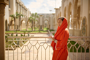 Beautiful Middle Eastern Muslim woman with head covered in hijab, standing with cupped hands at Hassan II mosque