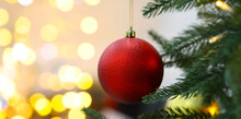 Red Bauble On Christmas Tree Branch Against Blurred Lights, Bokeh Effect. Banner Design With Space For Text