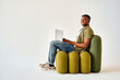 © HBS - Modern gadgets for freelance. Side view of happy handsome man typing on portable laptop while sitting on comfy design chair over white background. African american guy enjoying remote work in studio.