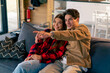 © Guys Who Shoot - Young couple in love together sitting on the sofa at home watching comedy film and laughing