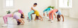 Group of children doing exercises at modern gymnastics studio. Woman trainer helps flexible sportive kid gymnast girls learn to stand correctly all together in backbend bridge position pose on floor