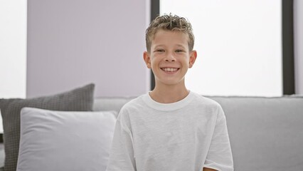 Wall Mural - Adorable blond boy, full of confidence and joy, flashing a cheerful smile while relaxing comfortably on the sofa at home.
