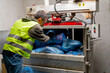 Shot from the back of a recycling plant employee in uniform putting bags of garbage into special press machine for waste disposal