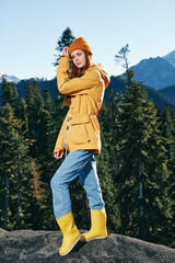 Wall Mural - Young woman with red hair full-length hiker in yellow raincoat and cap runs and walks on a mountain trip in the fall and hiking in the mountains at sunset freedom