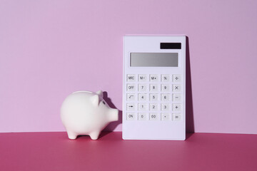 Wall Mural - White ceramic piggy bank and calculator on pink background with shadow