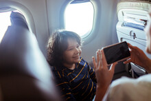 Happy Young Boy Posing For A Picture Taken By His Mother While Travelling And Flying Together On A Plane