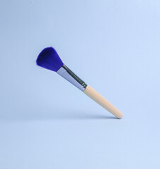 Wall Mural - makeup brush flying in antigravity on blue background with shadow. Levitation object in the air. Beauty and fashion concept. Creative minimalist layout