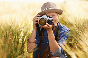 Wall Mural - Field, photographer and woman with a camera, portrait with nature, travel and memory with sunshine. Person, countryside or face with photography, outdoor and journey with adventure, picture or summer