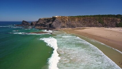 Wall Mural - Aerial video filming by drone of the sea bay and beach near the village of Odeceixe Alentejo Portugal. Tourists surfers in the water with rocks in the background.