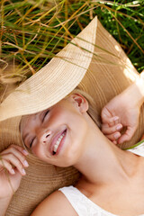 Poster - Woman, hat and relax on grass with peace, happiness and freedom in summer. Outdoor, fashion and girl lying on lawn with a smile on face for holiday, vacation or free time in nature with wellness