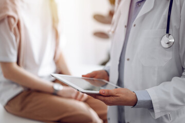 Doctor and patient discussing perfect health exam results. Friendly physician keeping tablet computer with her hands near a young woman. Medicine concept