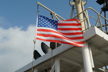 American Flag On The Wind Hanging On The Navigational Mast Near Exhaust Pipes Of Funnel On The Merchant Container Vessel During Mooring In The American Port.