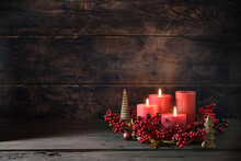 Third Advent Wreath With Red Candles, Three Are Lit, Decoration With Berries, Christmas Balls And Small Wooden Trees, Dark Rustic Background, Copy Space, Selected Focus