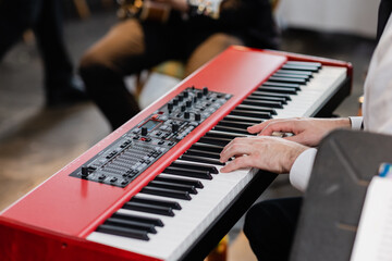 caucasian musician's hands on the keys of red keyboard playing jazz at event