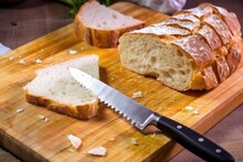 slicing ciabatta bread on a board with a serrated knife