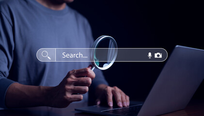 Search engine technology concept, Businessman holding magnifying glass and using laptop computer to Searching for internet information with web browser. Job search bar on website, Research online,