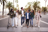 Fototapeta  - Diverse multicultural group young millennial friends walking along urban street palm trees. University people happy strolling outside on way to campus. Concept of cheerful students together. 