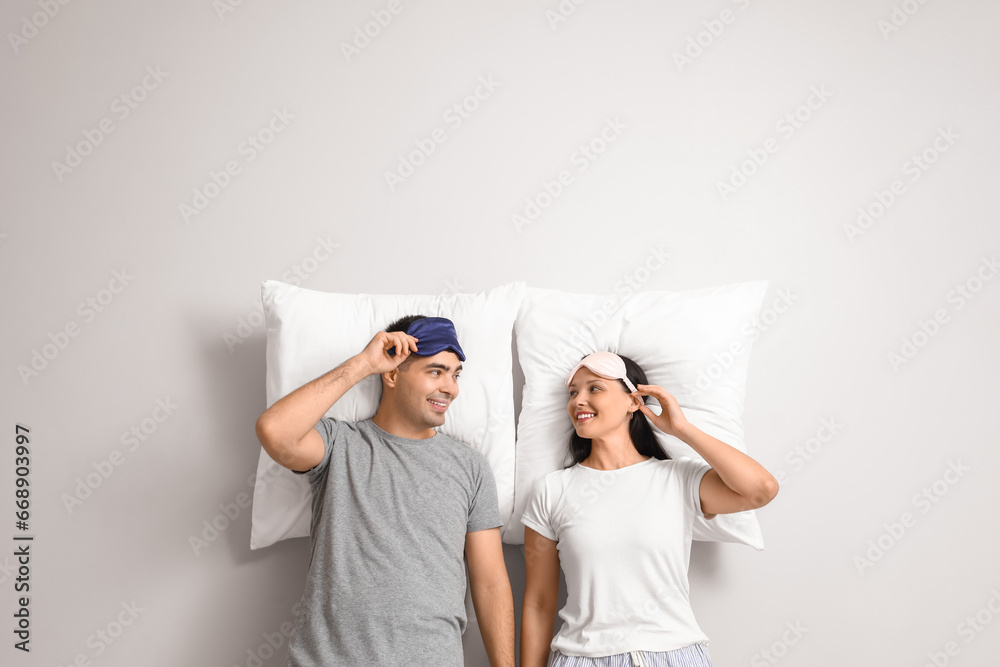 Young couple with sleeping masks and pillows on light background