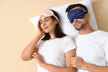 Sticker - Young couple in sleeping masks with pillow on beige background