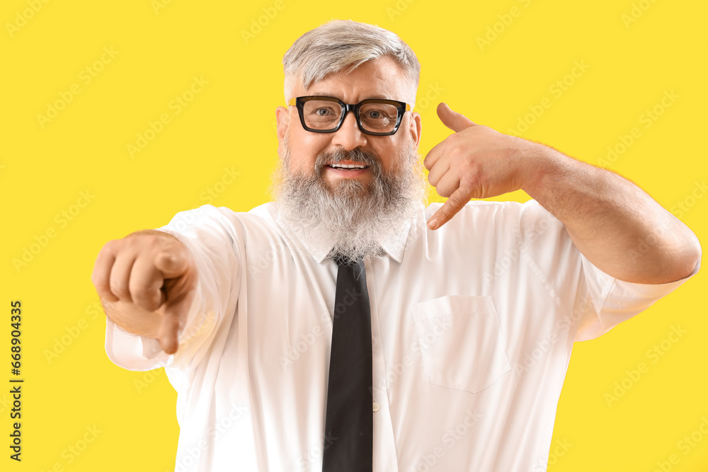 Mature businessman showing "call me" gesture on yellow background