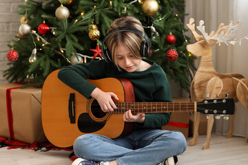 Sticker - Cute little boy in headphones playing guitar at home on Christmas eve