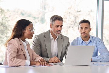 Executive business people using laptop working in office. Older male manager and professional international workers team looking at computer discussing tech project data at work meeting.