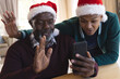 Happy african american father and son in christmas hats having smartphone video call