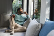© Wavebreak Media - Happy biracial man sitting on sofa and looking out window in sunny living room