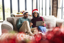 Happy Biracial Couple With Santa Hats Using Credit Card And Tablet In Living Room At Home
