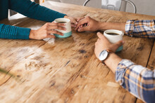 Hands Of Biracial Couple Sitting At Table With Coffee In Living Room At Home