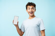 Portrait of happy teenage boy with braces holding mobile phone, showing screen isolated on blue background, mockup. Mobile app, technology concept  