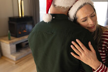 Happy Senior Caucasian Couple Wearing Santa Hats Embracing At Home At Christmas