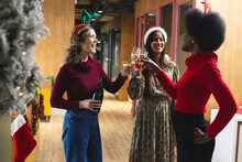Happy Diverse Female Colleagues Wearing Christmas Hats And Drinking Champagne In Office