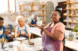© Wavebreak Media - Happy african american female potter glazing clay jug with others in pottery studio