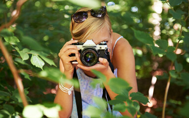 Wall Mural - Camera lens, shooting and photographer with woman in forest for relax, memory and travel photography. Summer, trees and adventure with person in nature for vacation, holiday and environmental tourism