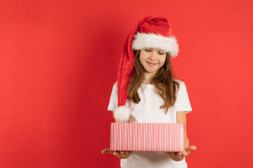 Sticker - Close-up portrait of a teenage girl in a santa hat and a gift in her hands on a red background, copy space