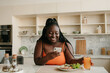 © gstockstudio - Beautiful plus size African woman using smart phone while enjoying healthy eating for lunch at home